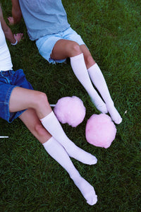 Three people sitting on green grass wearing matching Peara Socks Cotton Candy speckled pink knee-high compression socks, with two pink cotton candy balls on the grass between them.